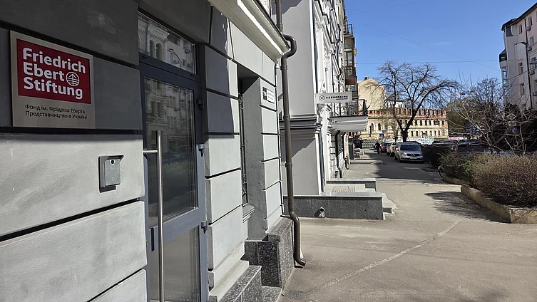 На фото зображено вхід до офісу Фонду ім. Фрідріха Еберта. Також можна помітити сучасний вхід до будівлі зі скляними дверима та міську вулицю з історисною забудовою.